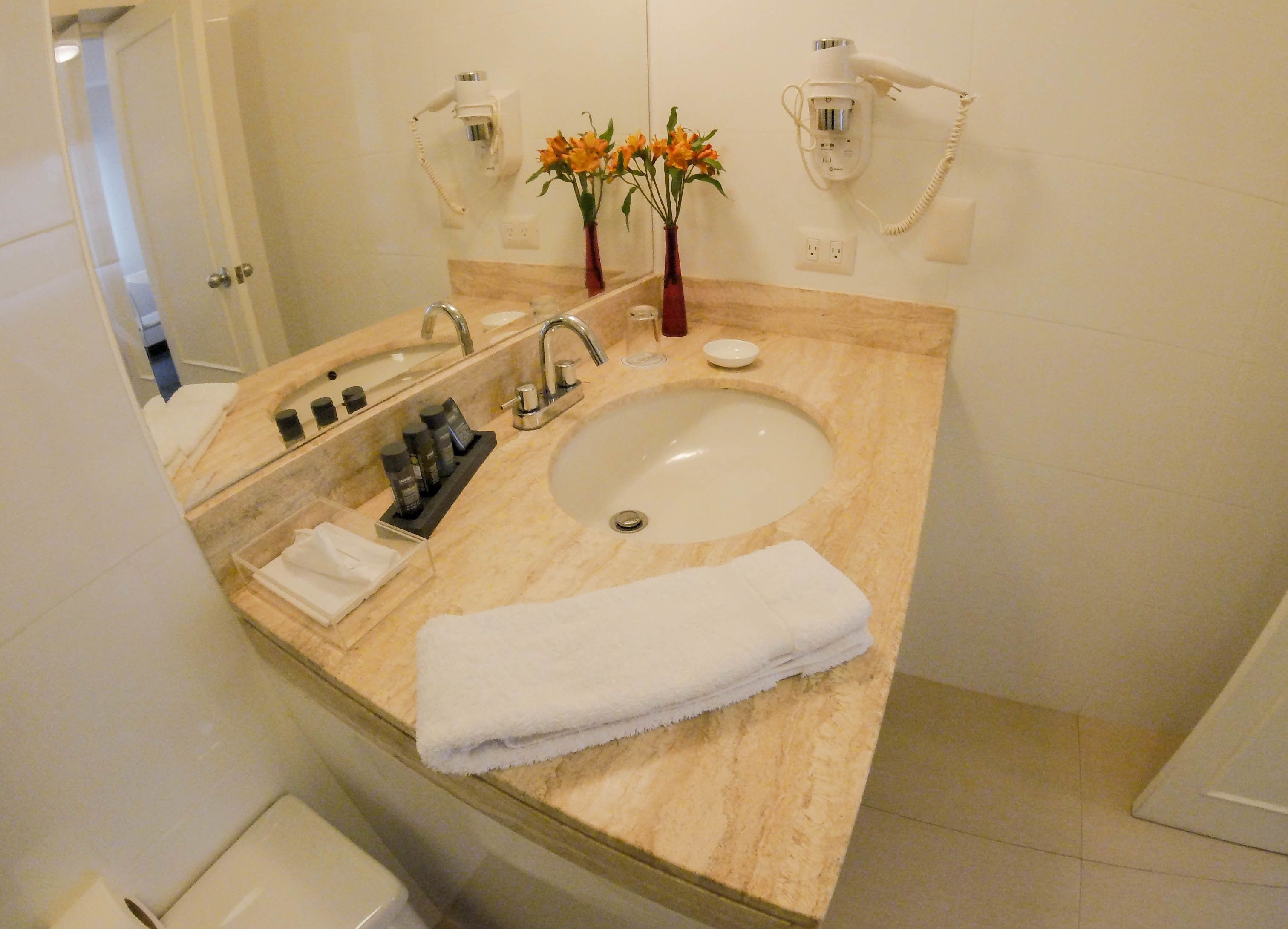 A bathroom with a marble sink, a mirror, a towel, and a vase with flowers.