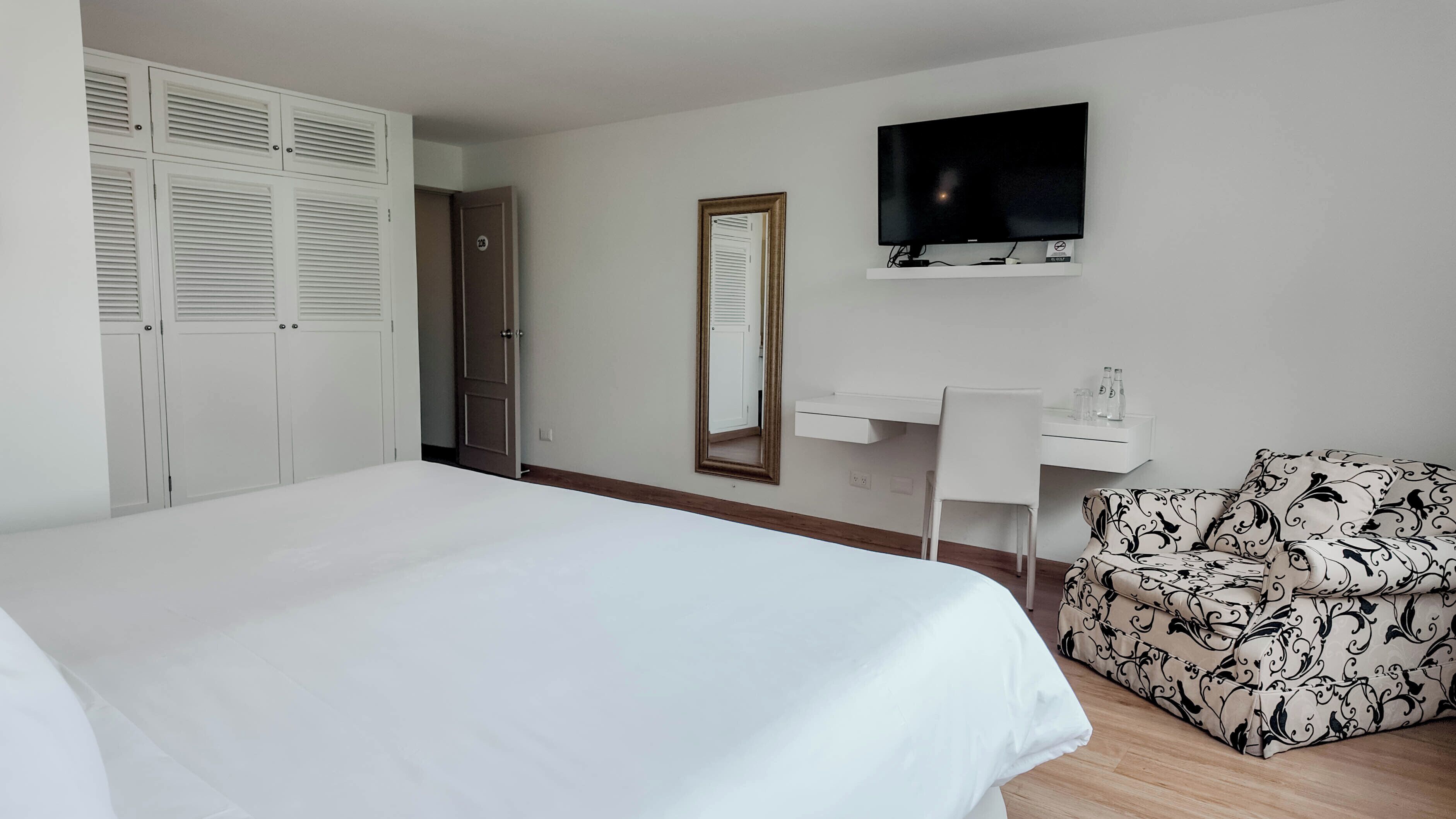 Habitación de hotel con una cama grande, un escritorio con silla, un televisor y un sofá estampado.