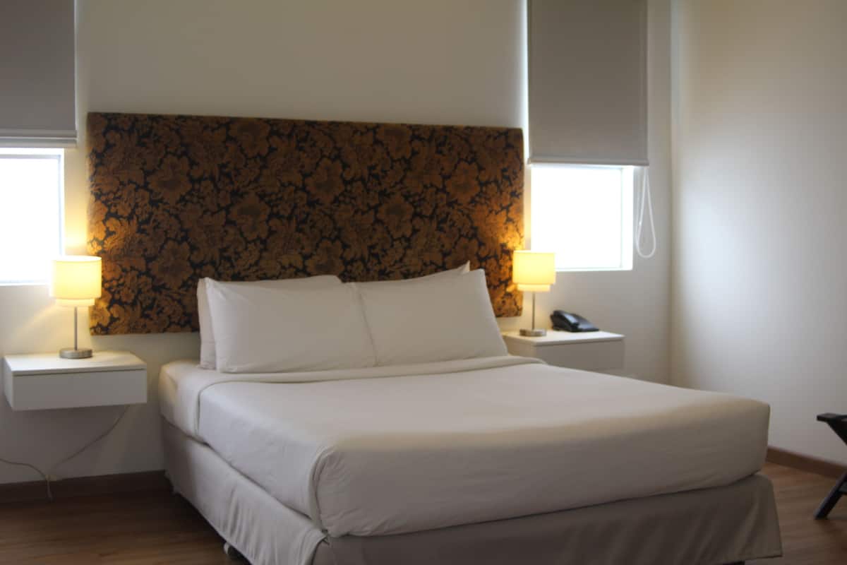 Una cama con ropa blanca de cama impecable, dos mesitas de noche con lámparas y un cabecero estampado con motivos florales.