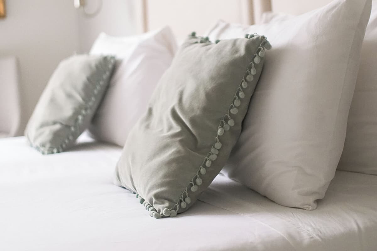 Una cama con ropa de cama blanca y dos almohadas, una con detalle verde.