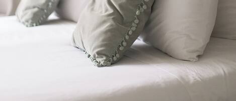 A bed with white bedding and two pillows, one with a green border.