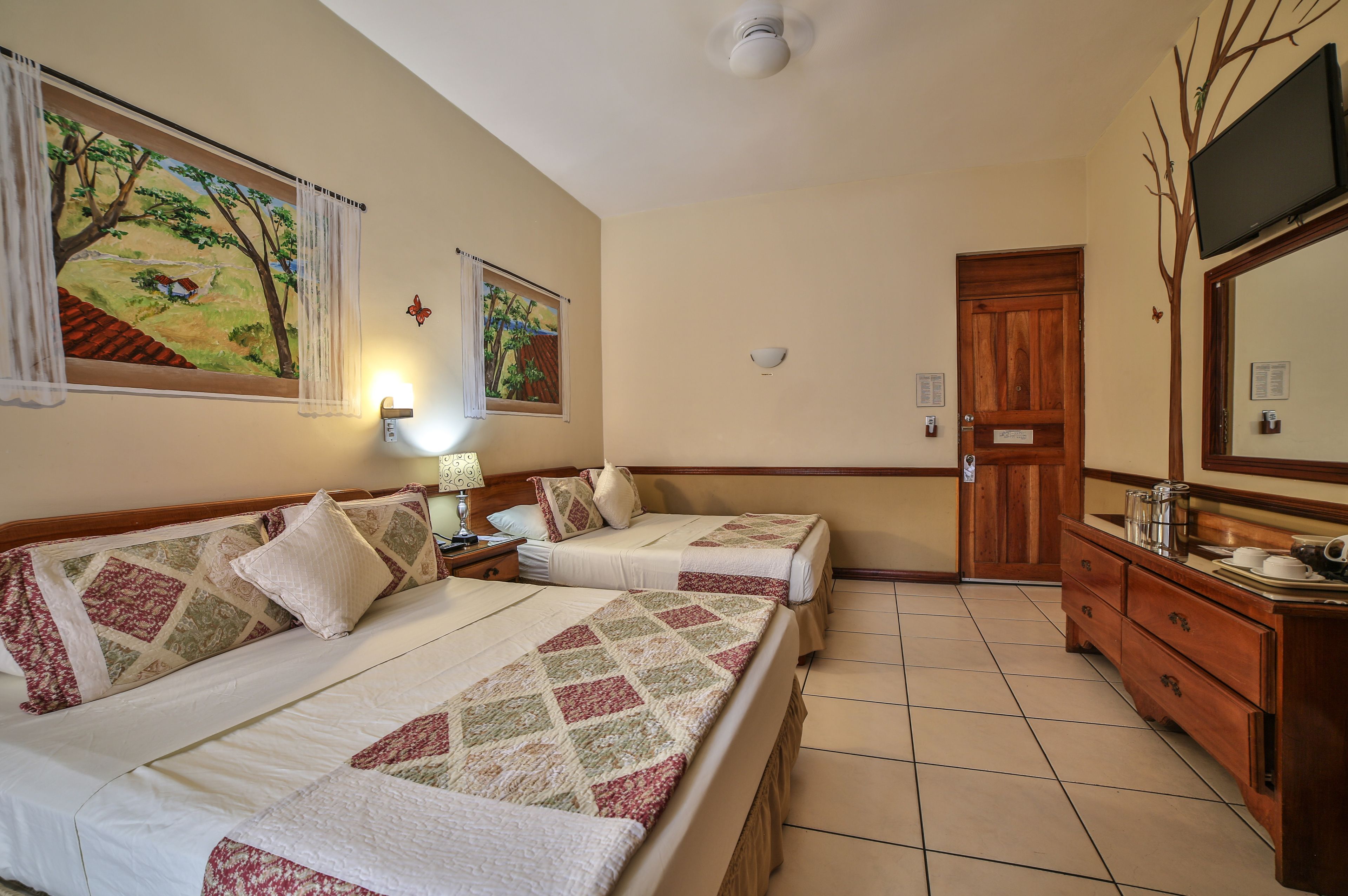 Habitación de hotel con dos camas, un aparador de madera, un espejo y dos cuadros en la pared.
