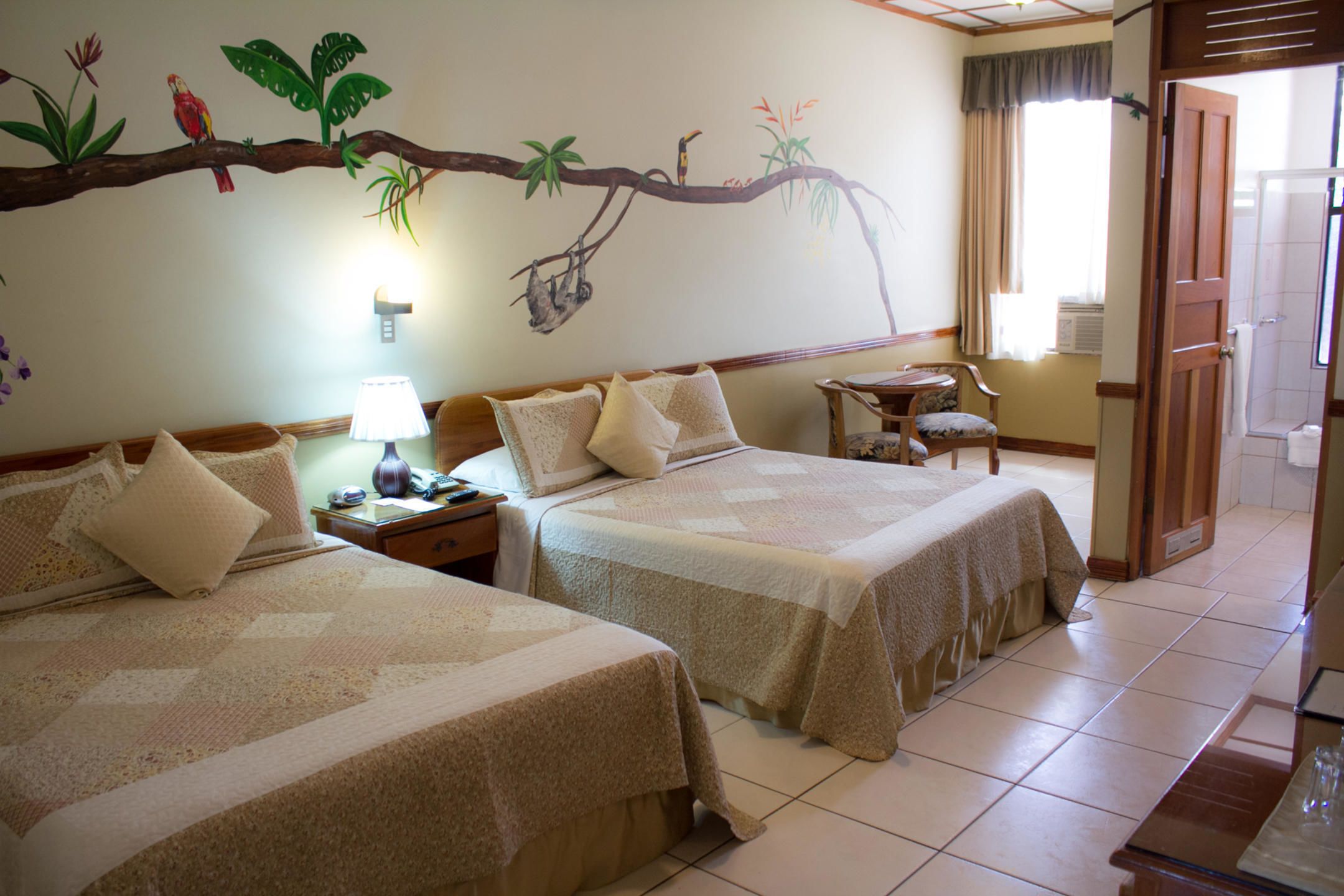 A hotel room with two beds, a nightstand, a lamp, a chair, and a shower area.