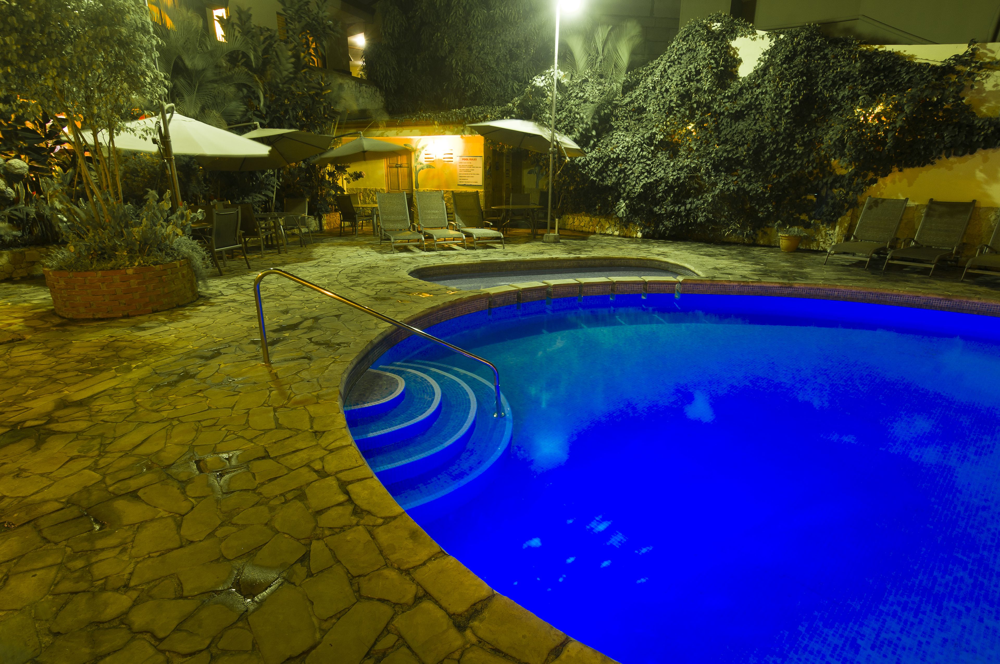 A swimming pool with a stone deck, surrounded by lounge chairs and umbrellas.