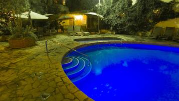 A swimming pool with a stone deck, surrounded by lounge chairs and umbrellas.