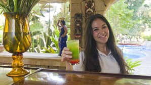 A person holding a drink at a bar with a decorative vase and a statue in the background. - Adventure Inn (Ulloa)
