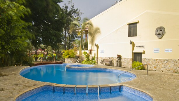 A swimming pool with a stone deck, surrounded by trees and a building with a stone facade. - Adventure Inn (Ulloa)