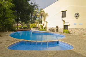 A swimming pool with a stone deck, surrounded by trees and a building with a stone facade. - Adventure Inn (Ulloa)