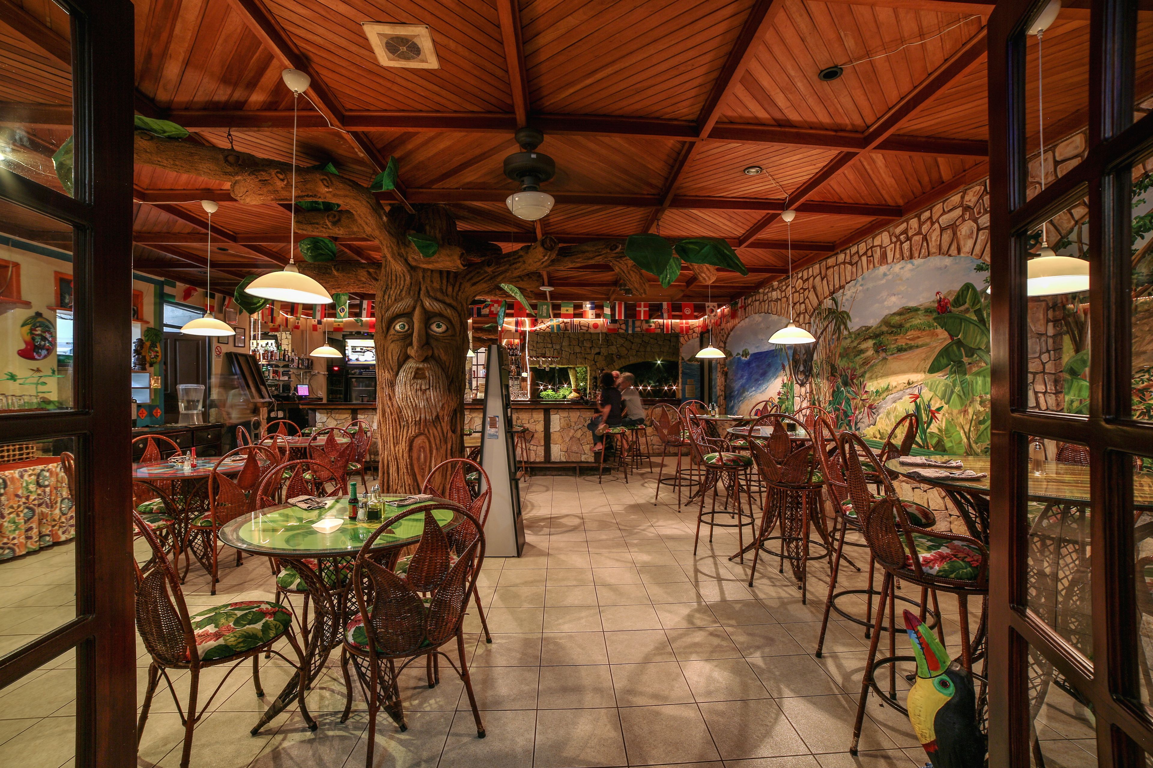 Um restaurante com teto de madeira, cadeiras estofadas verdes e um mural na parede.