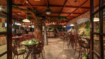 Un restaurante con techo de madera, sillas con cojines verdes y un mural en la pared.
