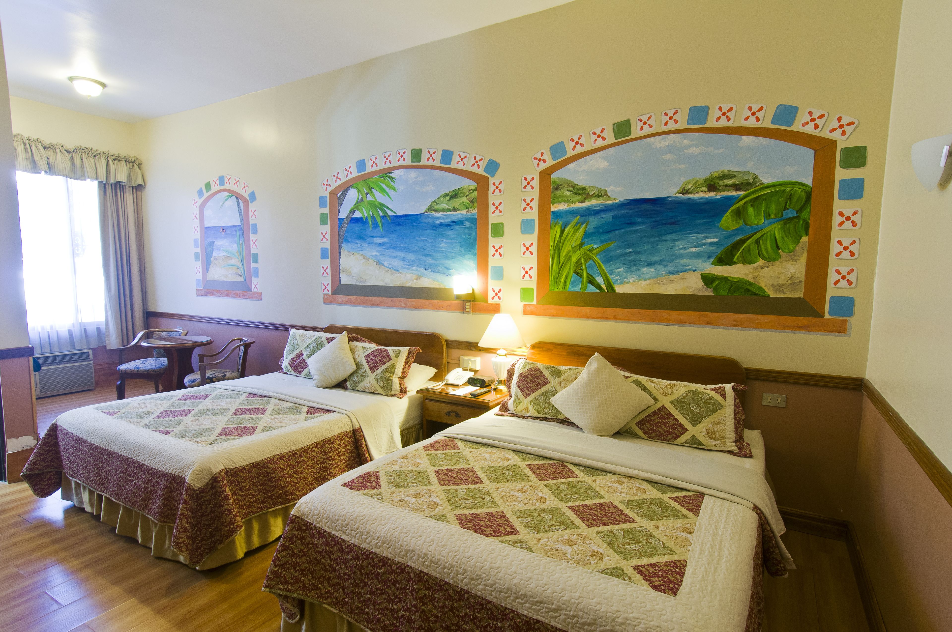 Une chambre d’hôtel avec deux lits, un bureau et une chaise. Les murs sont ornés de tableaux et il y a une fenêtre avec des rideaux.