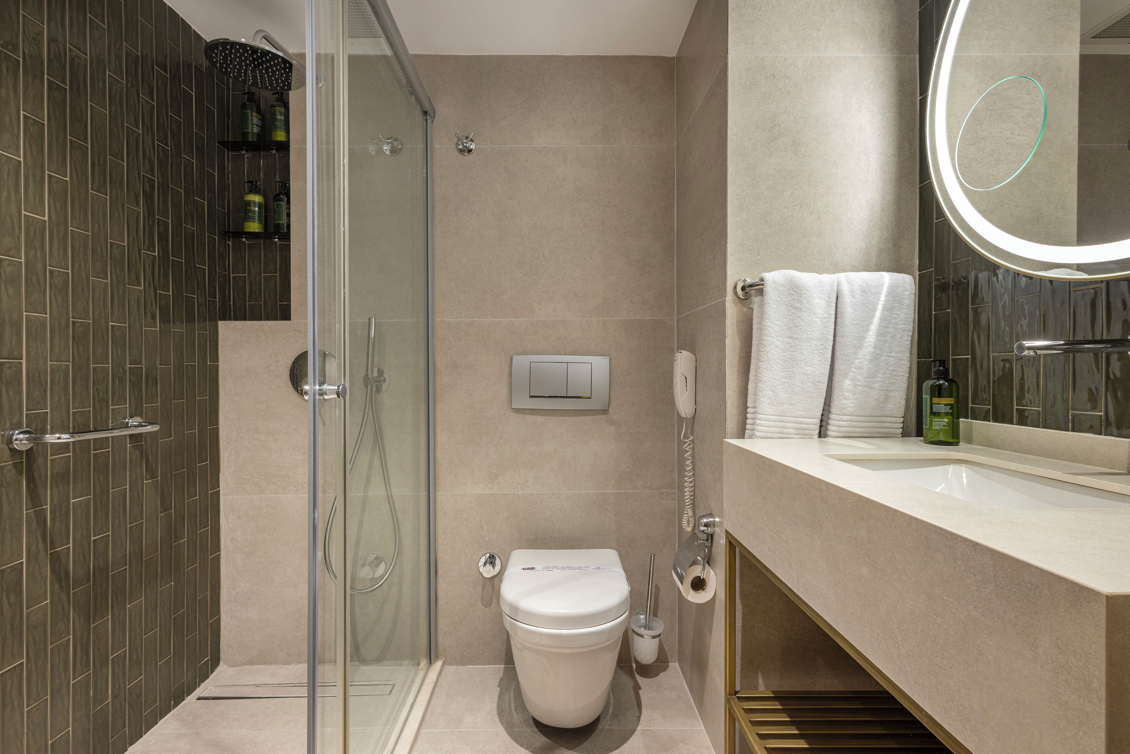 Un baño moderno con cabina de ducha de vidrio, inodoro, tocador con espejo y toallero.