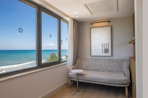 Una habitación con vista al océano, un sofá gris, una mesita blanca pequeña y una obra de arte enmarcada en la pared.