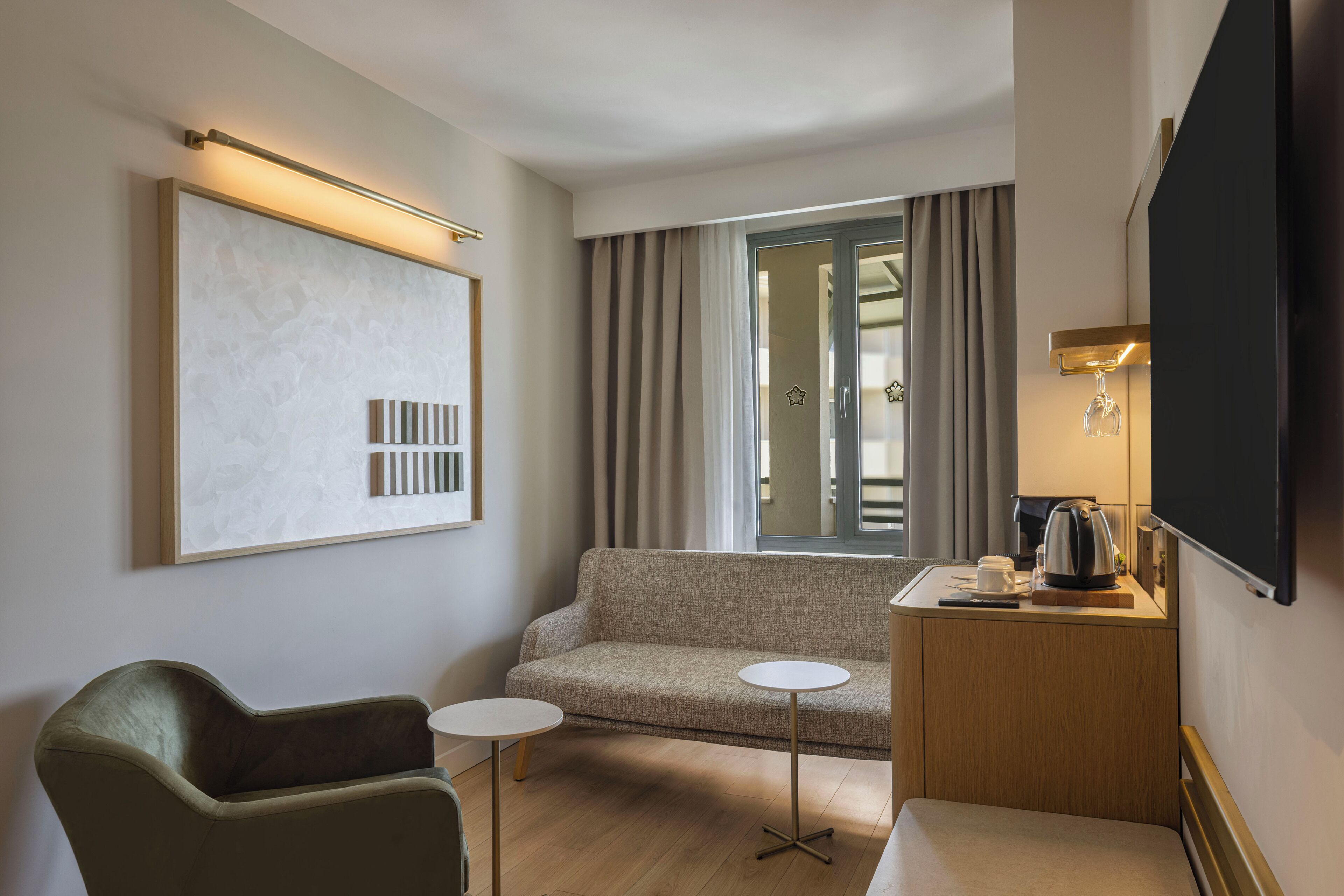 A hotel room with a sofa, two small tables, a coffee maker, and a TV.