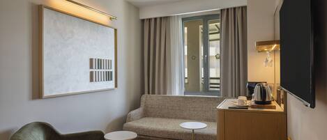A hotel room with a sofa, two small tables, a coffee maker, and a TV.