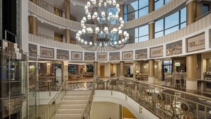 Een hotellobby met meerdere niveaus, voorzien van een imposante kroonluchter, marmeren vloeren en een centrale trap.