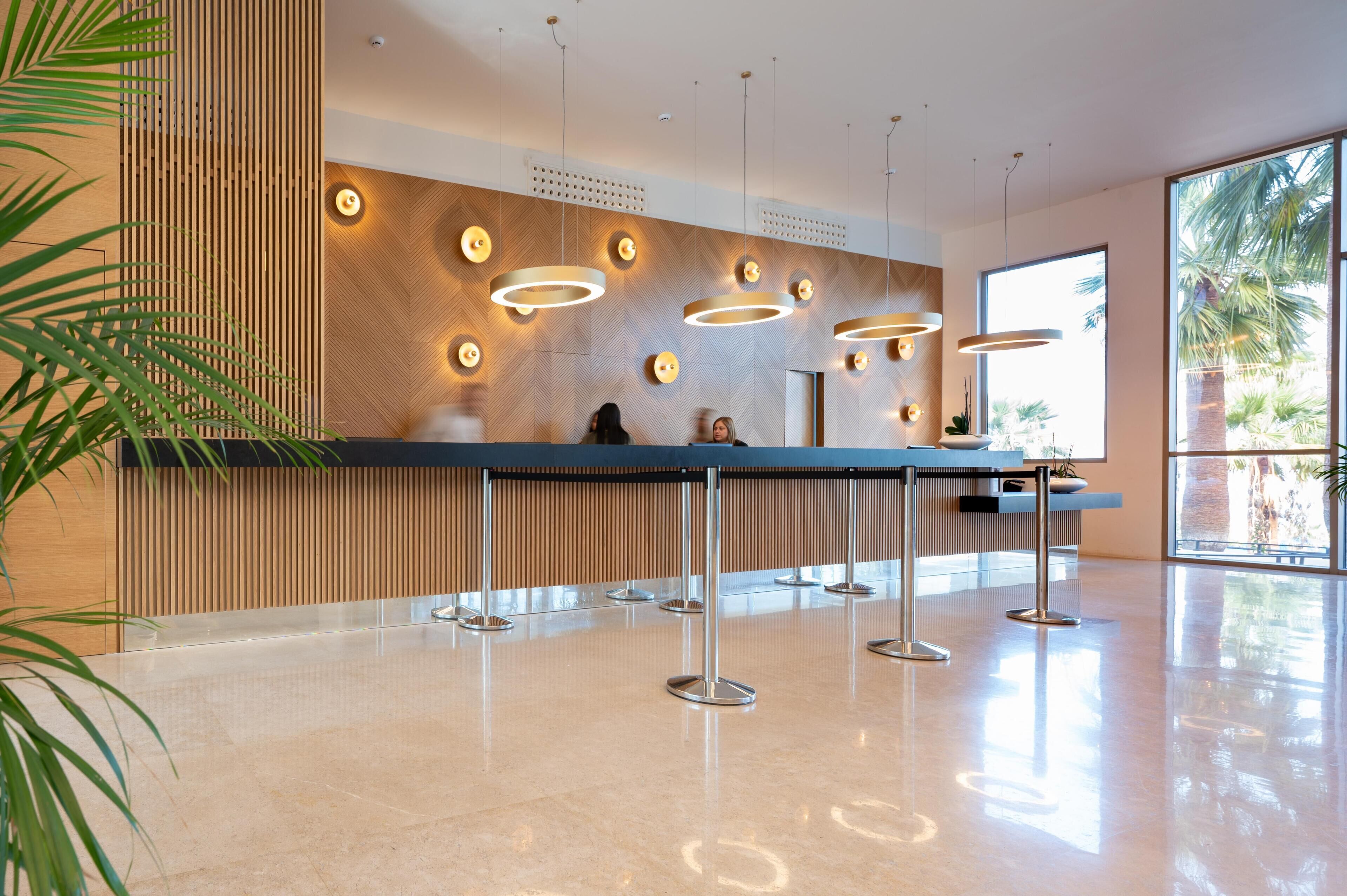 Un área de recepción moderna con un panel de madera en la pared, múltiples lámparas colgantes y un piso de mármol pulido.