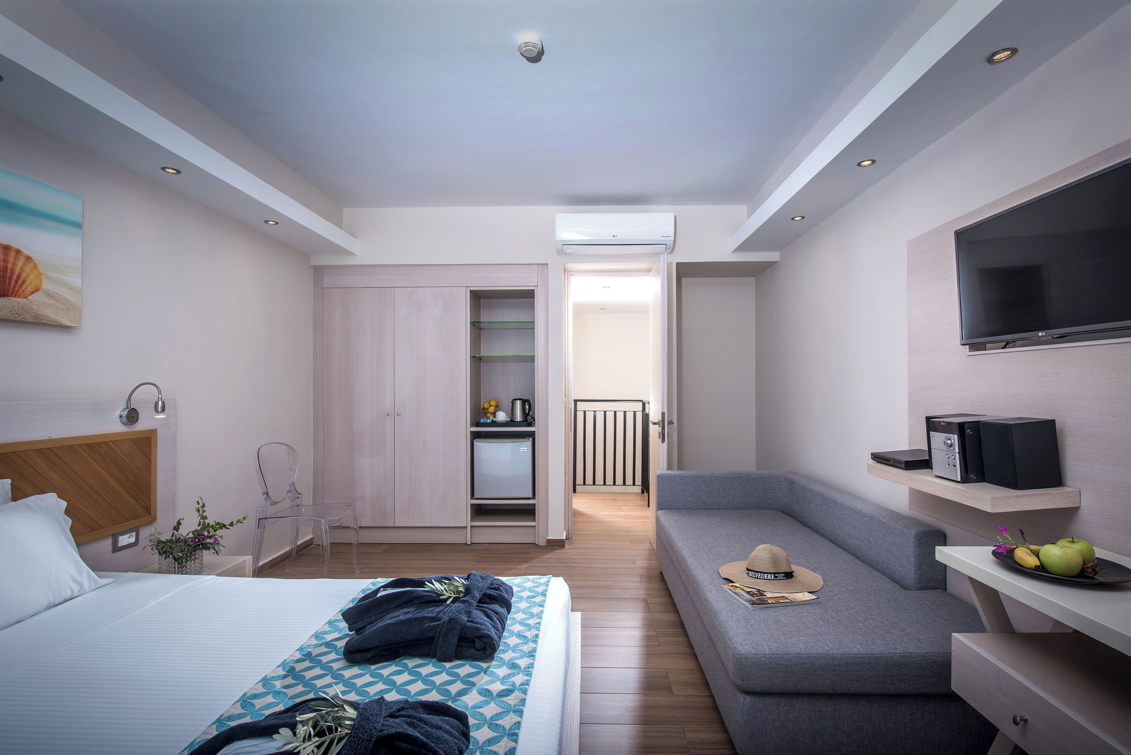Una habitación de hotel moderna con cama, zona de estar, televisor y kitchenette.
