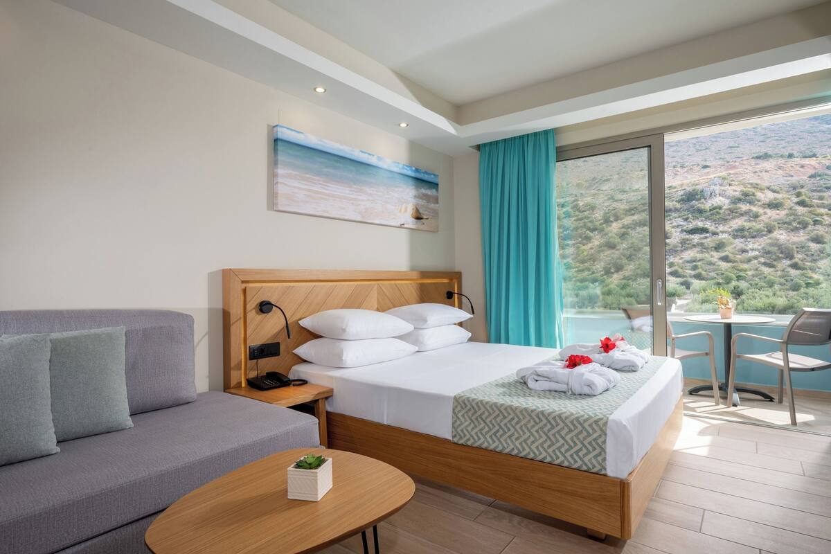 Una habitación de hotel con cama, sofá, una mesita y un balcón que ofrece vistas del paisaje.