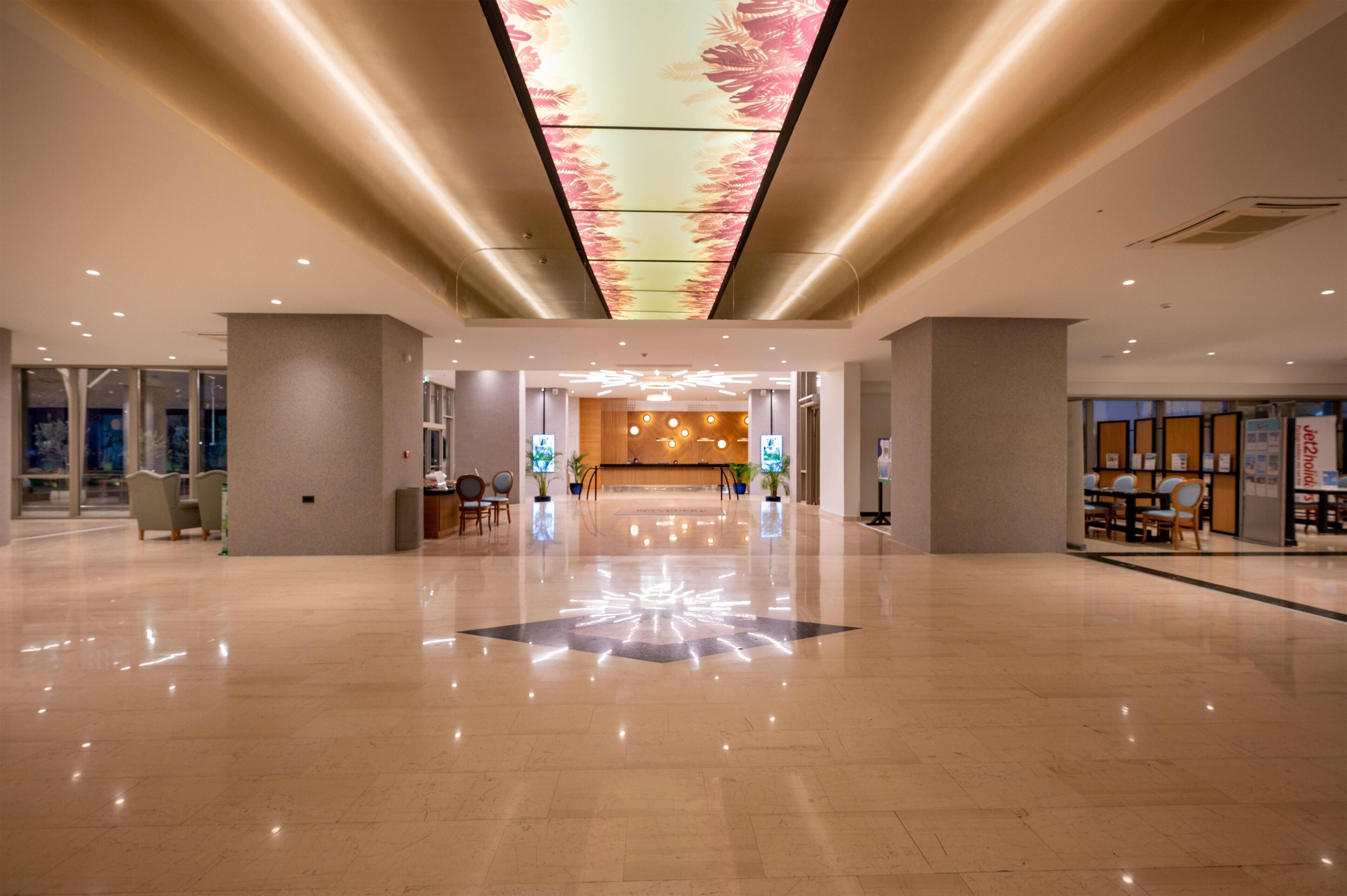 Un vestíbulo amplio con piso pulido, una recepción central y un techo con diseño de luces florales.