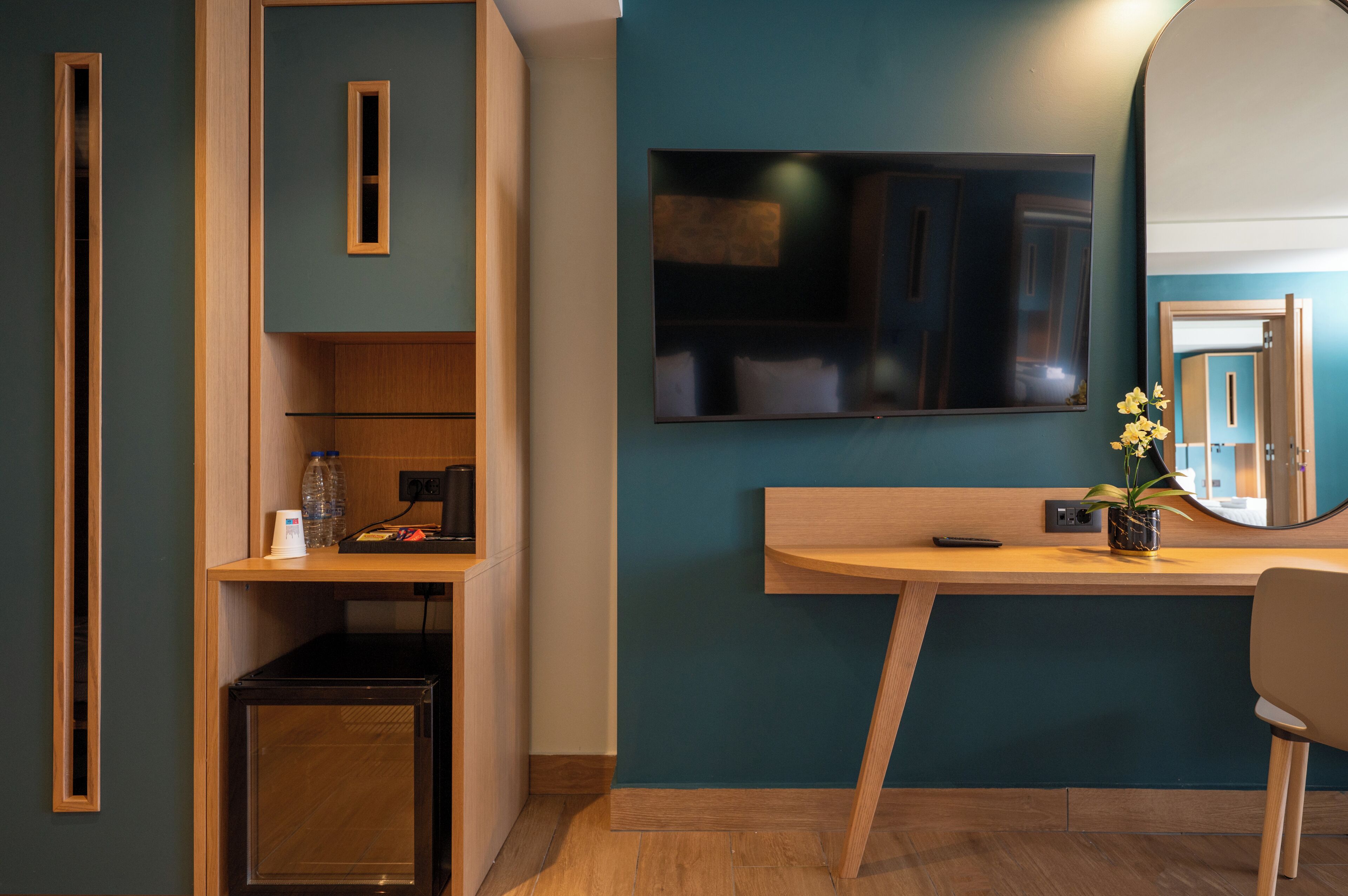 Une chambre moderne avec un bureau en bois, un miroir et un téléviseur fixé au mur.