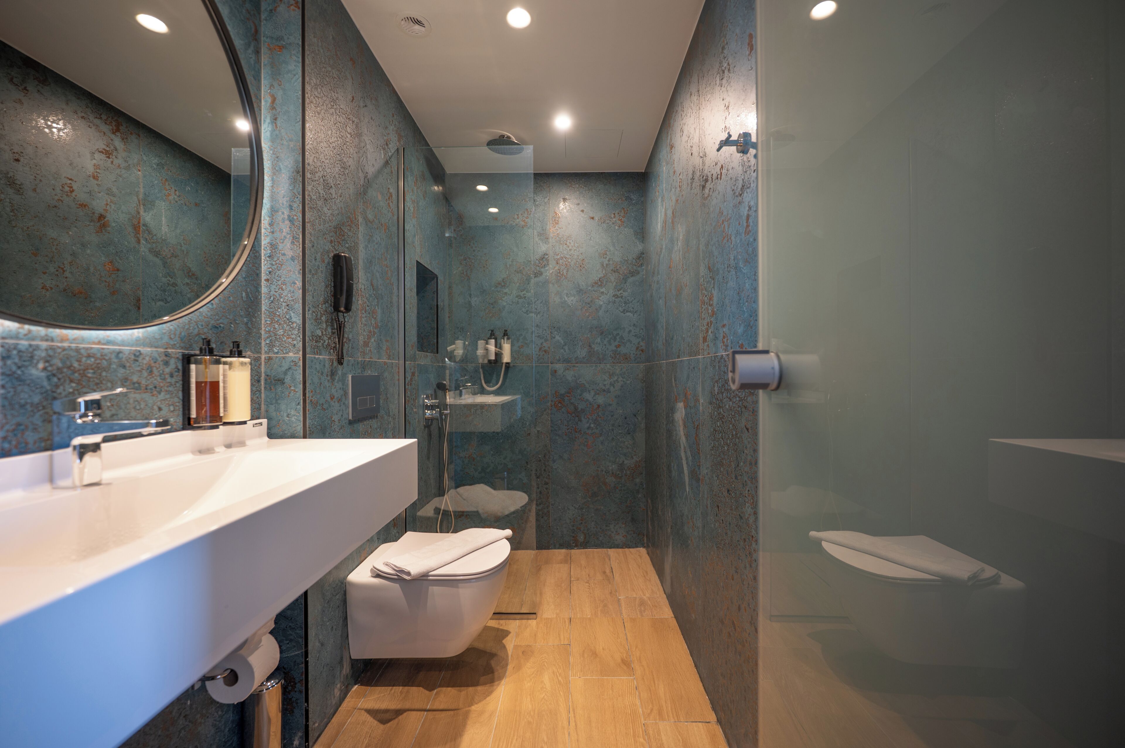 Une salle de bain moderne avec un grand miroir, un lavabo blanc et une douche séparée par des parois en verre.