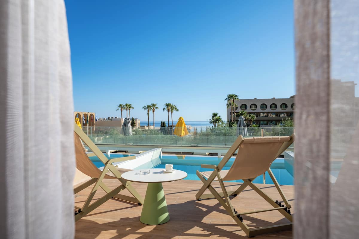 Zona de piscina con sillones reclinables y una mesa, con vistas a un cielo azul despejado y un edificio de diseño circular.