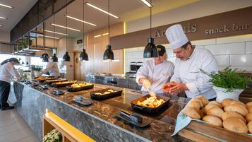 A modern kitchen with chefs preparing food, a marble countertop, and a sign for 'Aris snack bar'.
