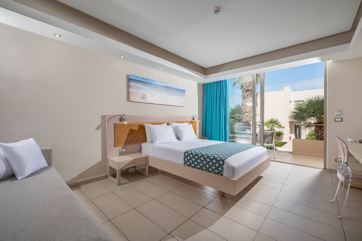 Habitación de hotel moderna con una cama grande, una mesita de noche, un escritorio y vistas al exterior.