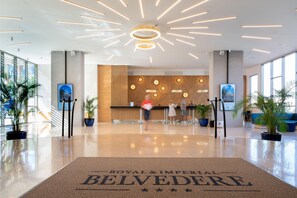A modern hotel lobby with a reception desk, potted plants, and a large welcome mat. - Royal & Imperial Belvedere Resort - All inclusive (Hersonissos)
