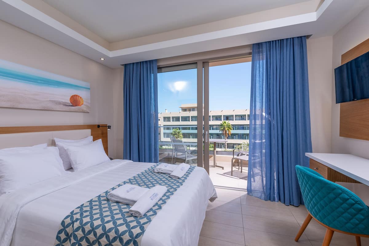 Habitación de hotel con cama, escritorio, silla y balcón con vistas a edificios.