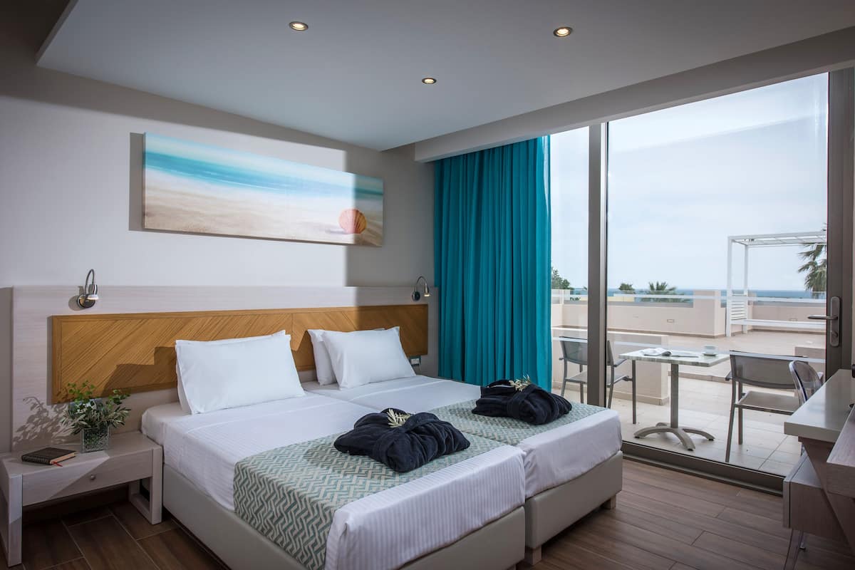 Habitación de hotel con una cama grande, un escritorio y un balcón con vistas al mar.