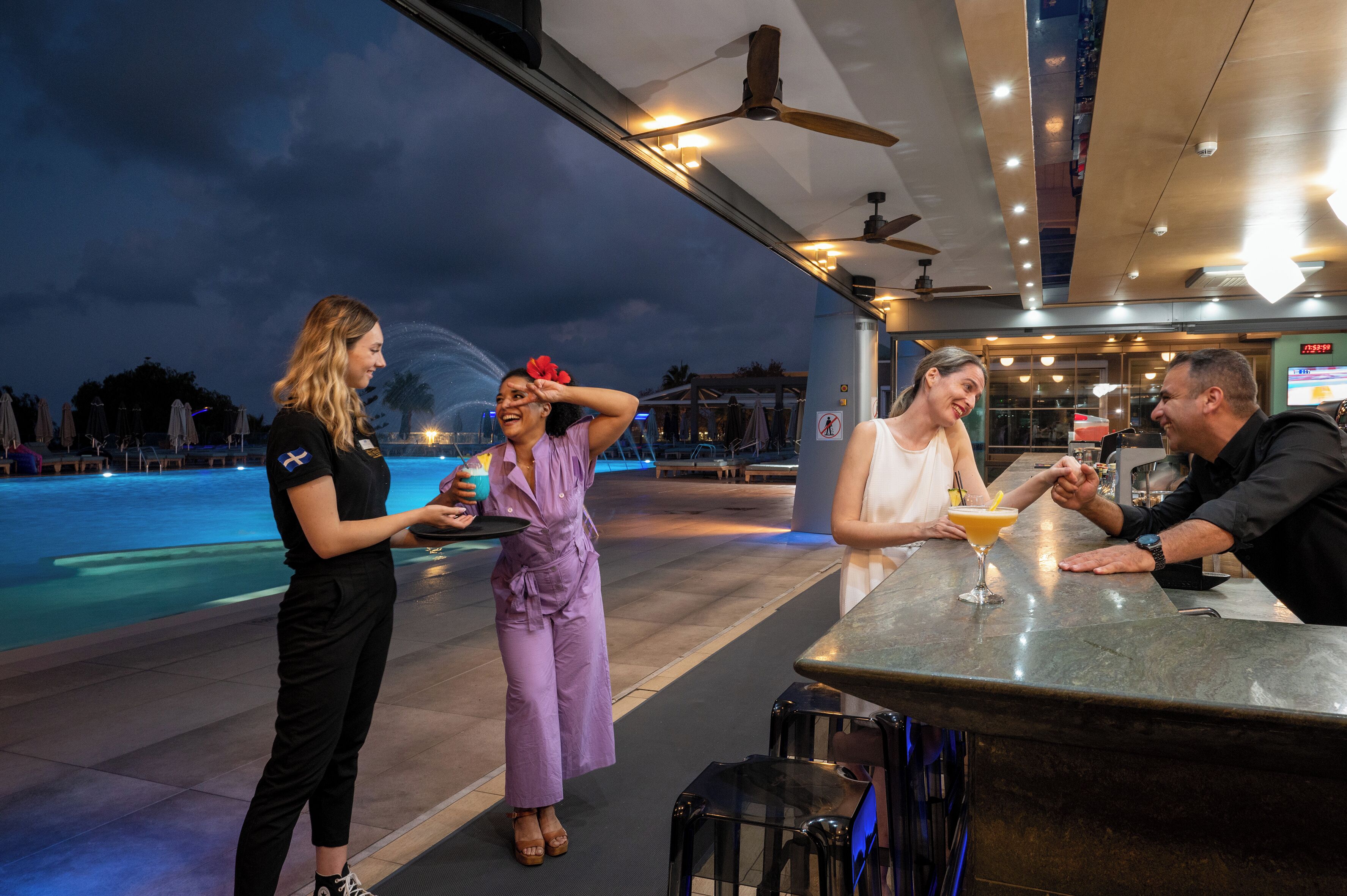 A bar area with a pool view, bar stools, and a ceiling fan.