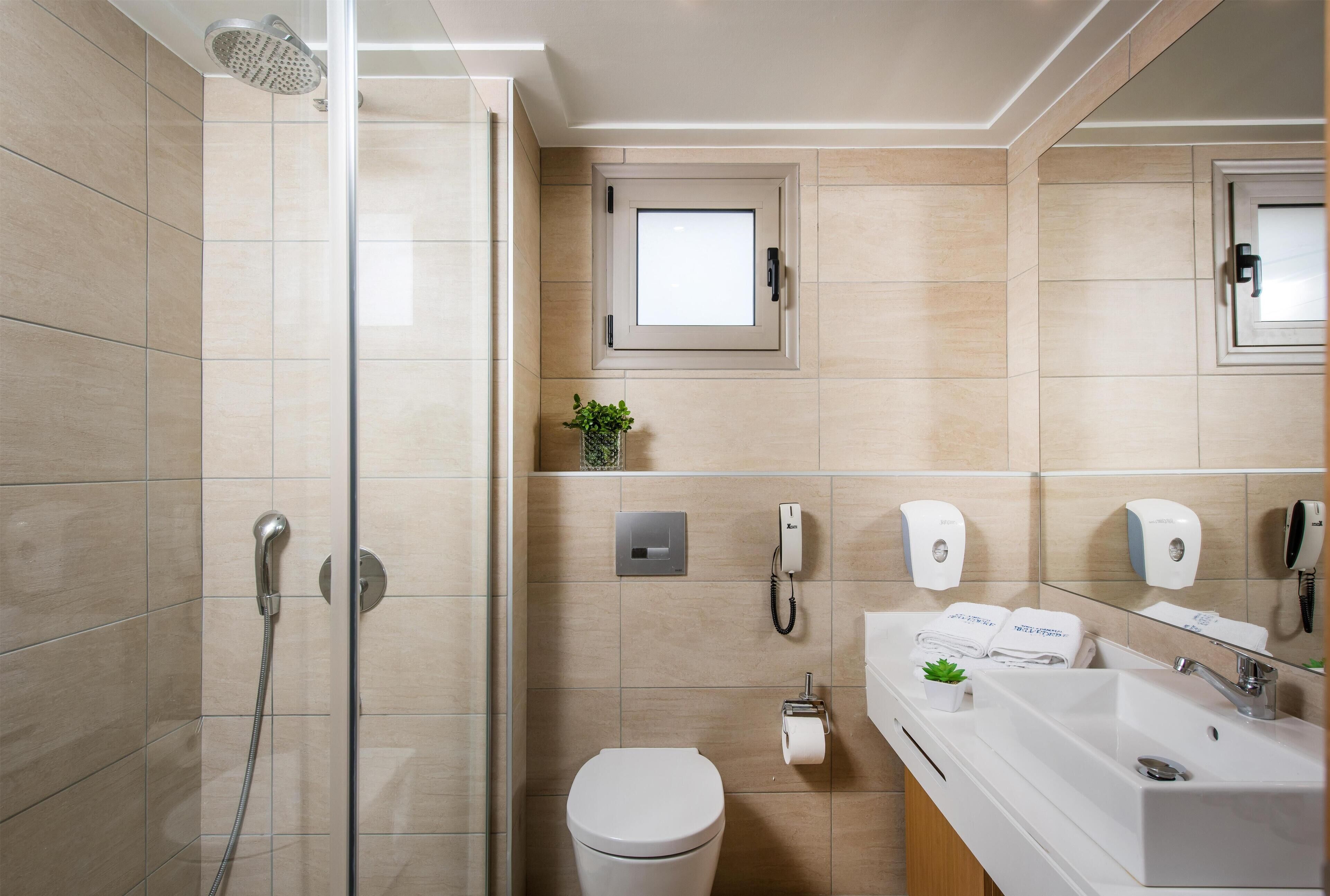Un baño moderno con cabina de ducha de vidrio, inodoro, lavabo con espejo y una pequeña ventana.