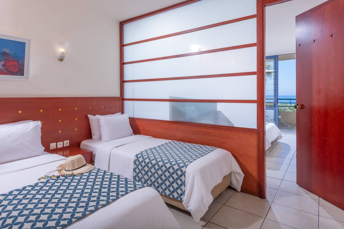 Habitación de hotel con dos camas, cabecero de madera, un cuadro en la pared y vistas a través de un ventanal.