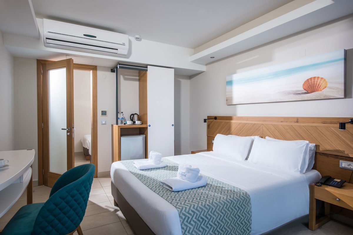 Habitación de hotel con cama, escritorio, silla, unidad de aire acondicionado, un cuadro de concha y cabecero de madera.