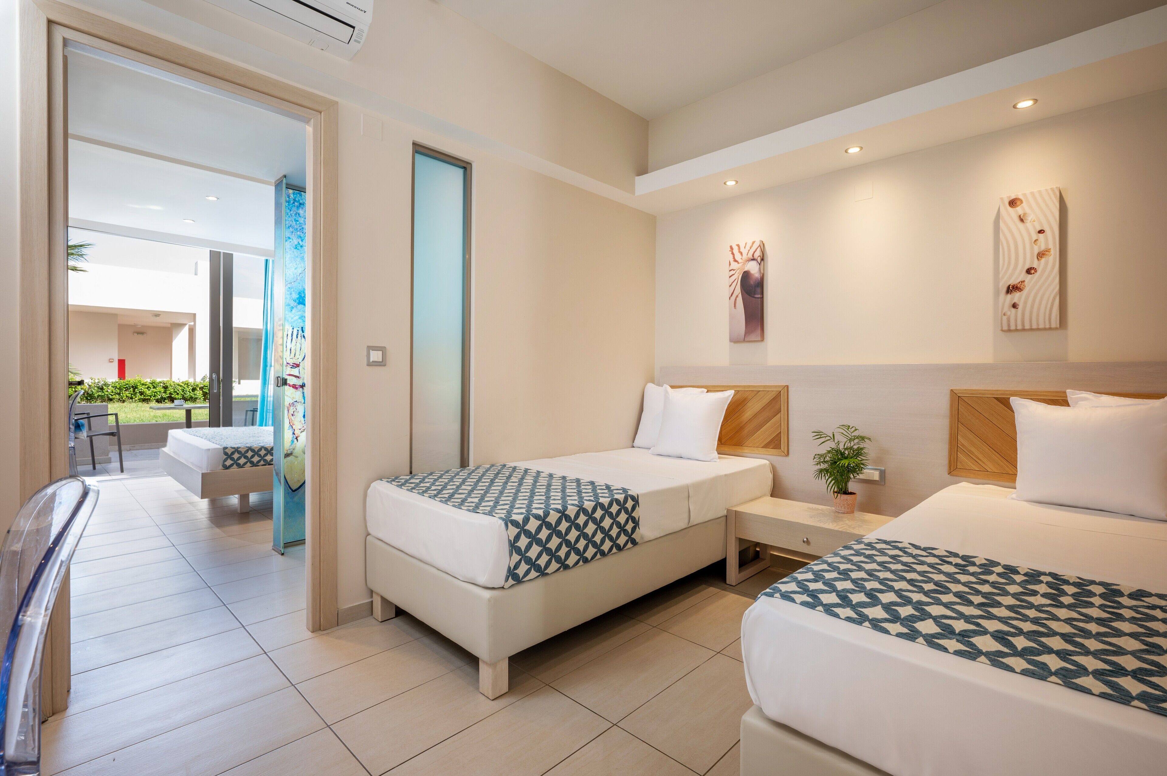 A hotel room with two beds, a small table, and a potted plant.