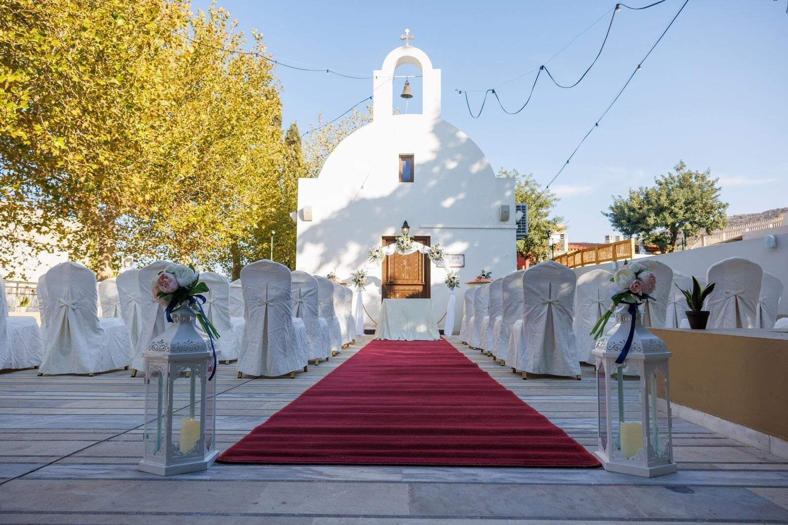 A church with a red carpet aisle leading to the altar, surrounded by white chairs with floral arrangements.