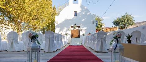 A church with a red carpet aisle leading to the altar, surrounded by white chairs with floral arrangements.