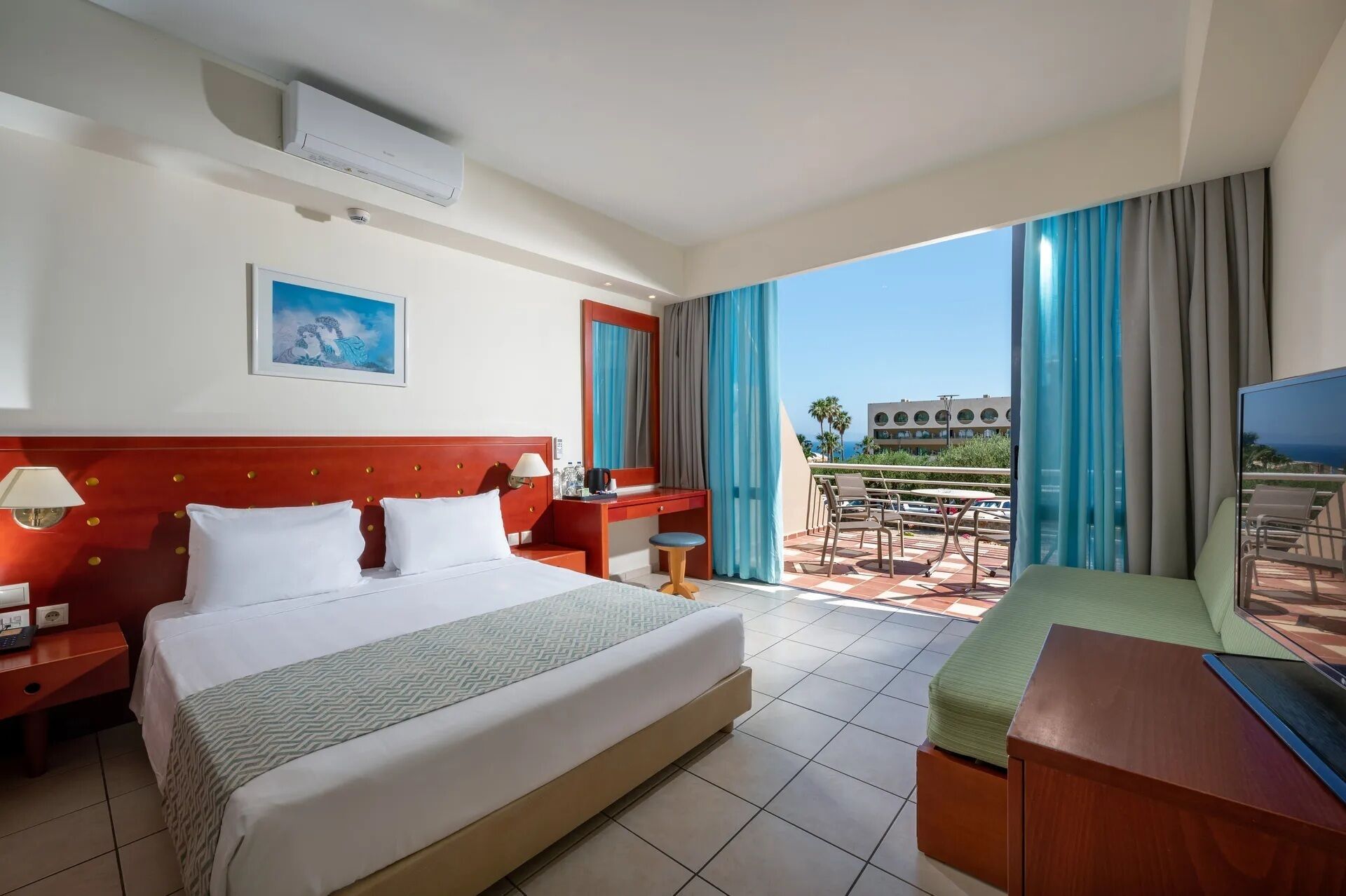 A hotel room with a large bed, a desk, and a balcony with a view of the ocean.
