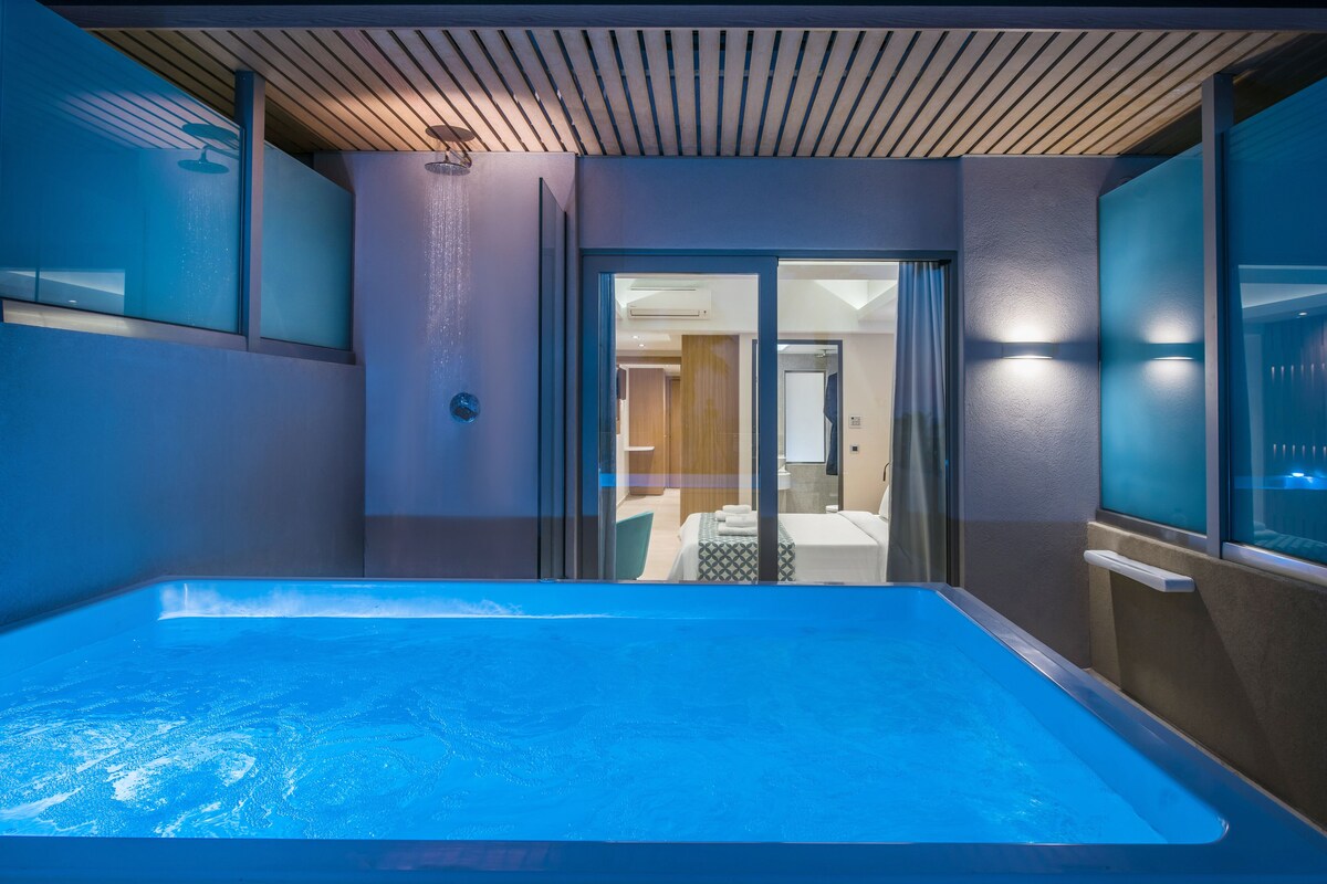 Un baño moderno con una bañera grande, zona de ducha y puerta de cristal que da a un dormitorio.