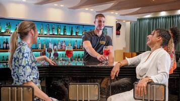 Zona de bar con un bartender sirviendo bebidas a los clientes sentados.