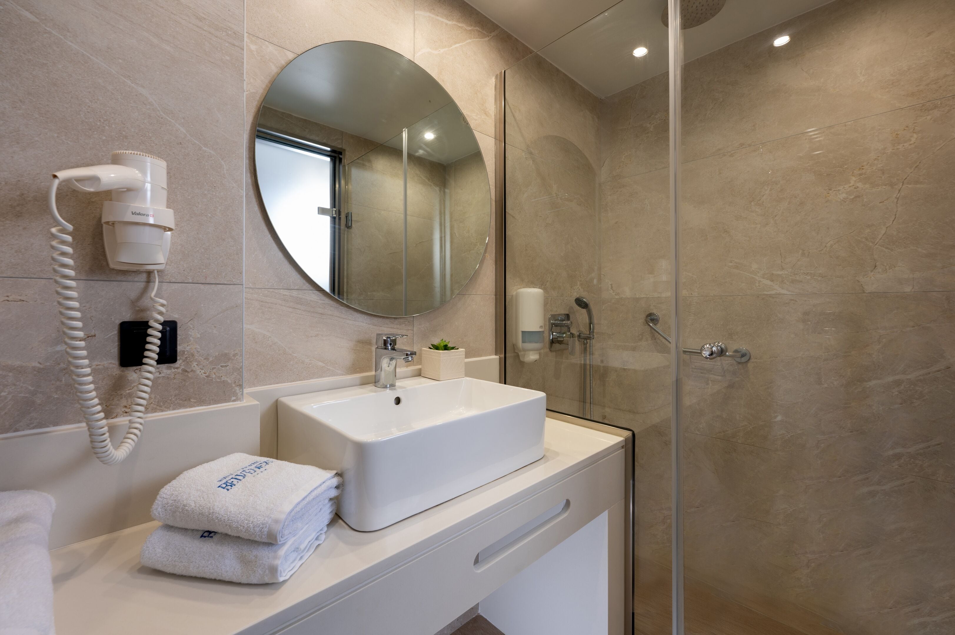 A modern bathroom with a large mirror, a sink, a hairdryer, and a glass shower enclosure.