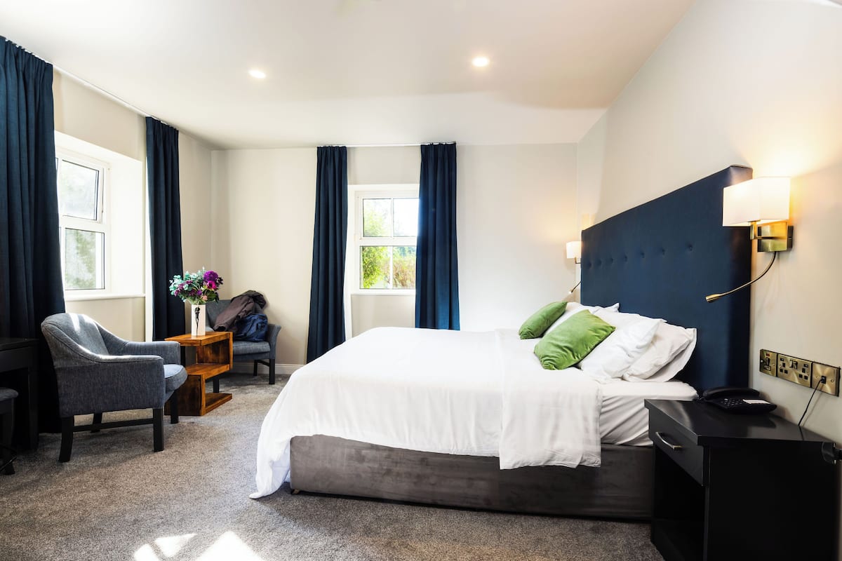 A hotel room with a bed, a chair, a nightstand, and a window with curtains.