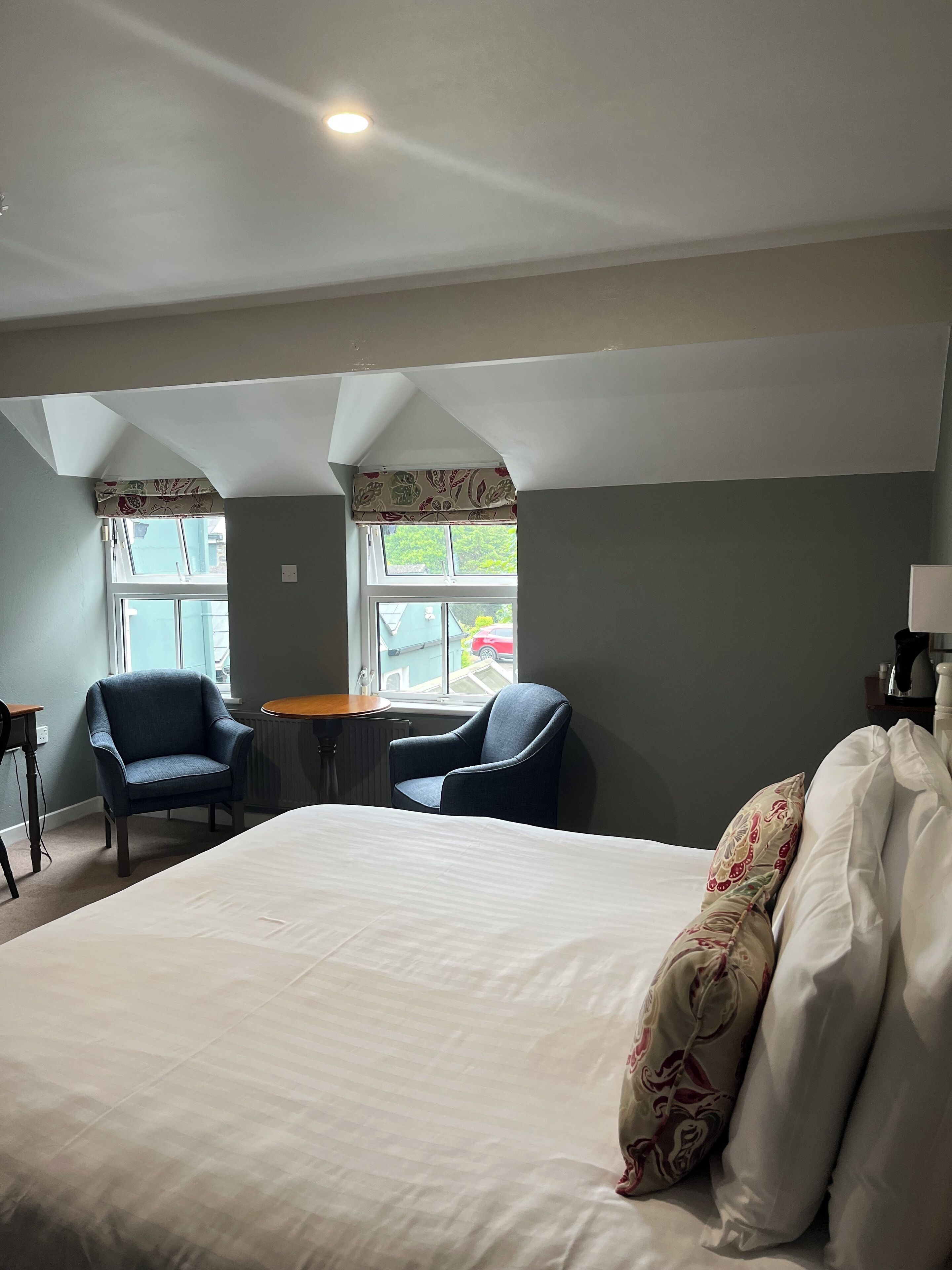 A hotel room with a large bed, two armchairs, a small table, and a window with a view of the street.