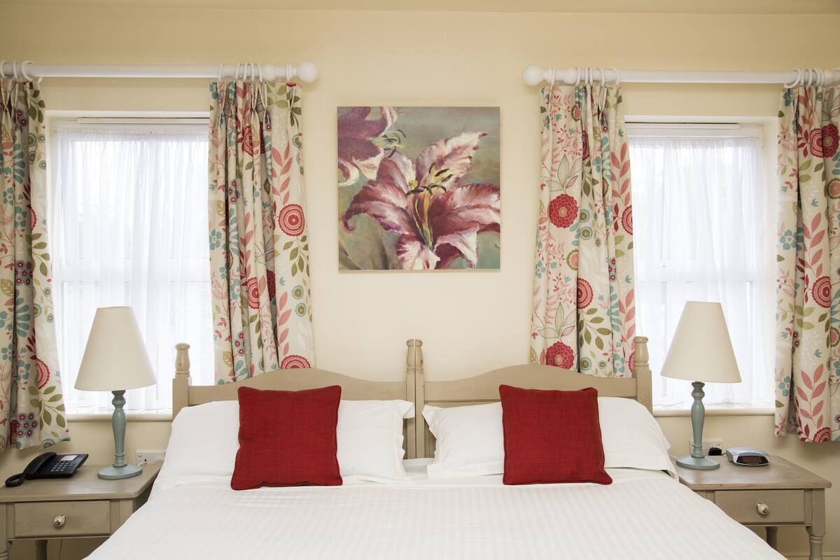 A neatly made bed with red pillows, two bedside lamps, and a telephone on the nightstand.