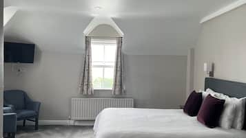 A bedroom with a bed, a chair, a TV, a window with curtains, and a radiator.