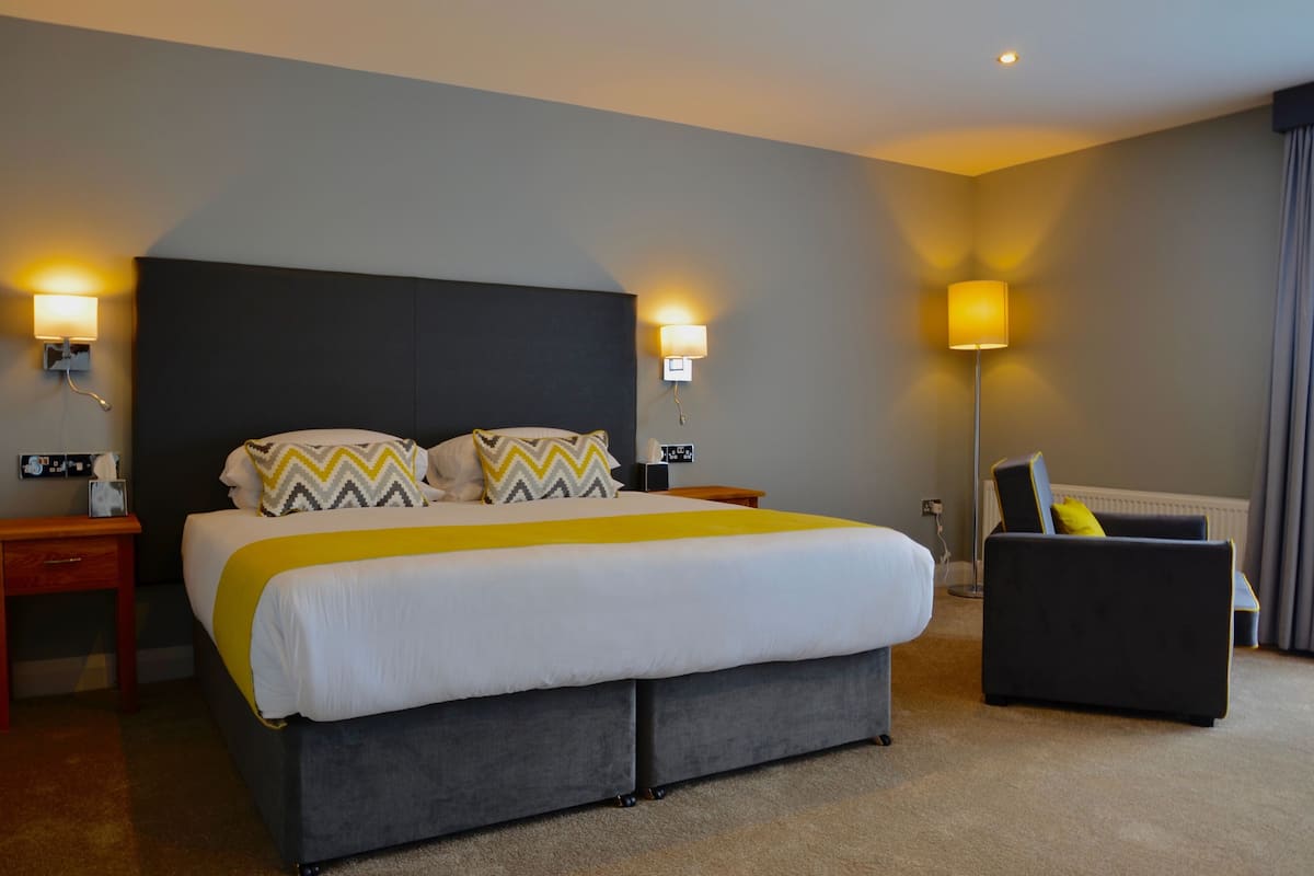 A hotel room with a large bed, two bedside tables, a floor lamp, and a dark armchair.