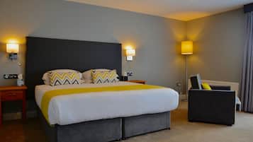 Una habitación de hotel con una cama grande, dos mesitas de noche, una lámpara de pie y un sillón oscuro.