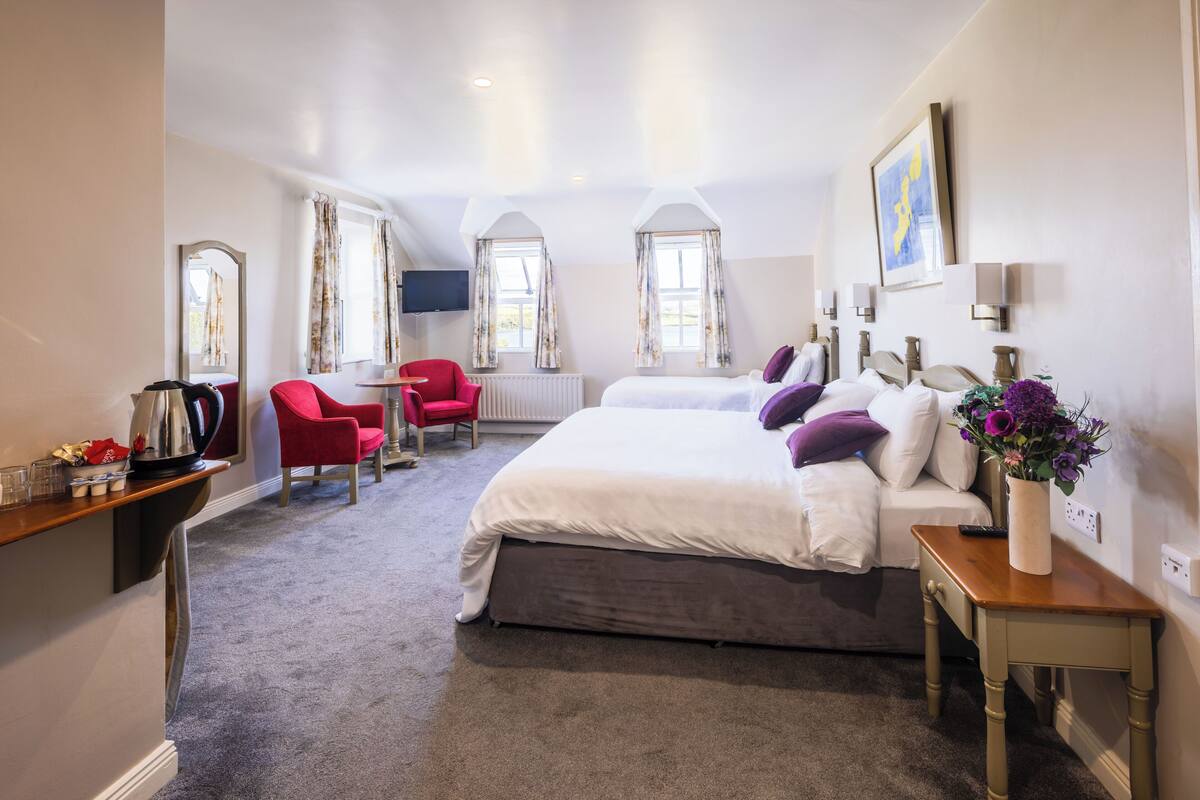 A bedroom with a large bed, a red chair, a small table, and a vase of flowers.